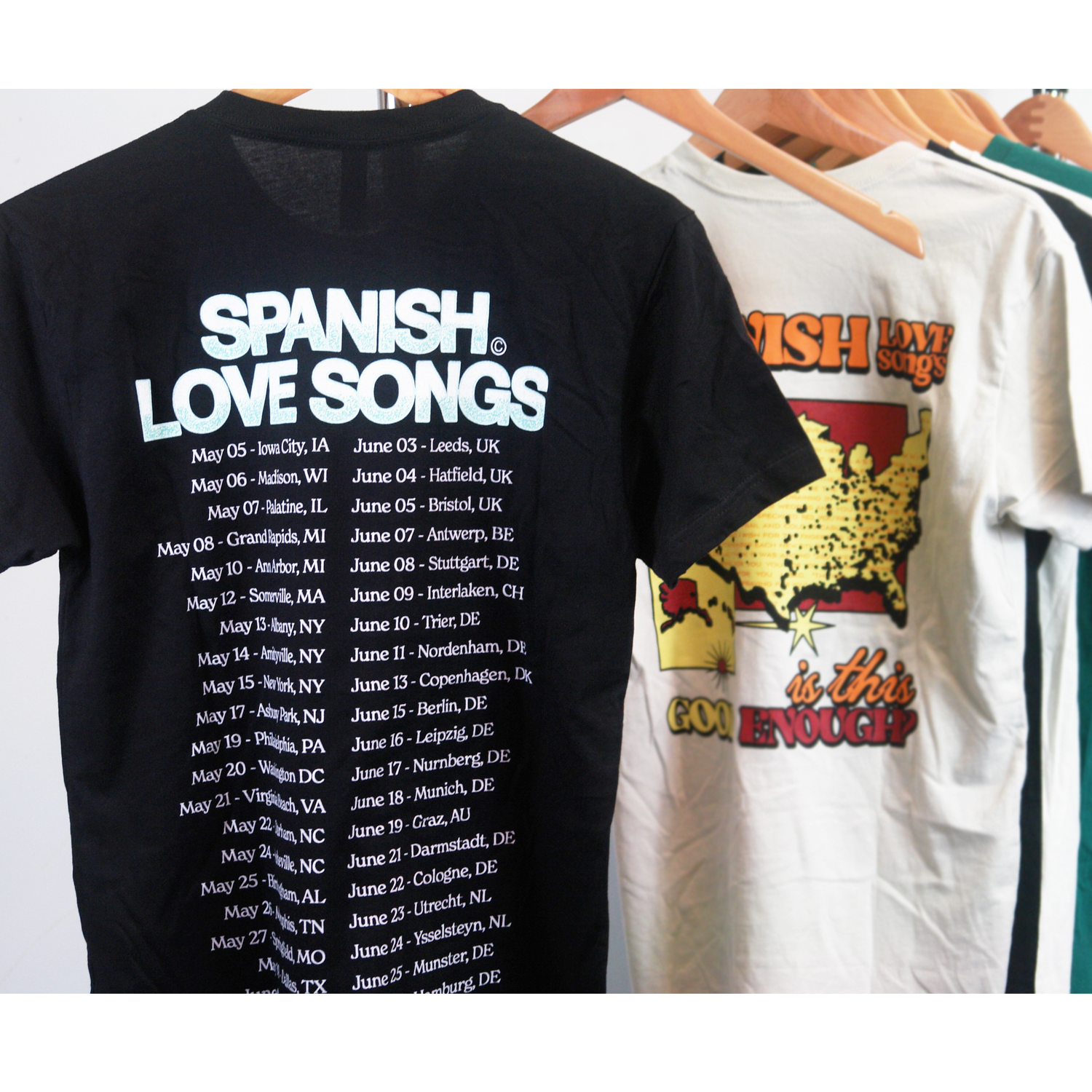 image of the back of a black tee shirt hanging. the back of the tee full print that says at the top spanish love songs and a list of the 2022 spring tour dates and locations below