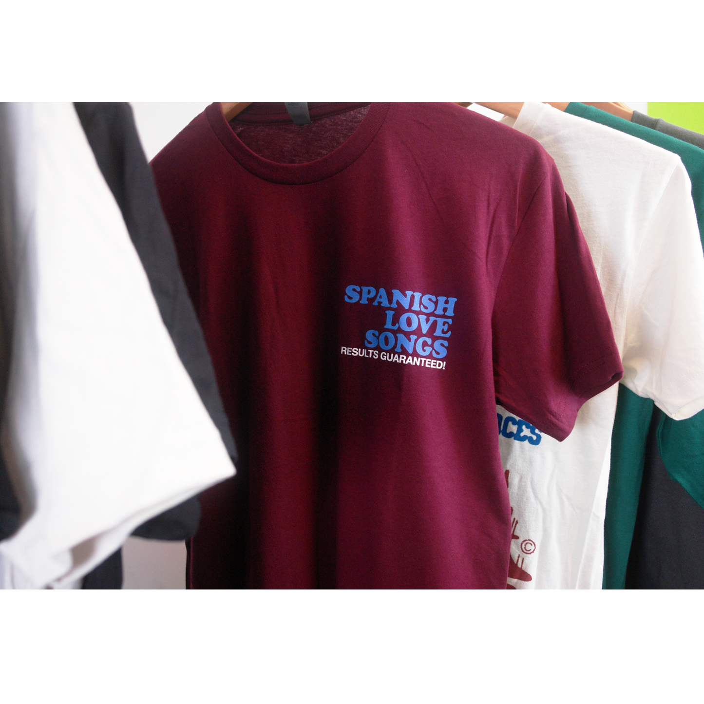 image of the front of a maroon tee shirt on a white background. front of tee has a small chest print on the right. stacked in blue says spanish love songs and below in white says results guaranteed!